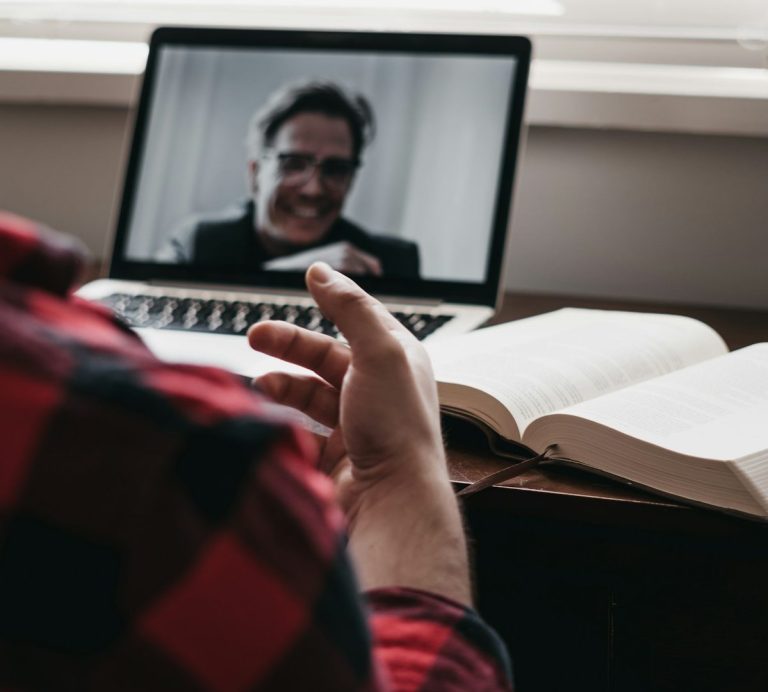 Person spricht mit jemandem über Laptop, Notizbuch und offene Bücher sind sichtbar.
