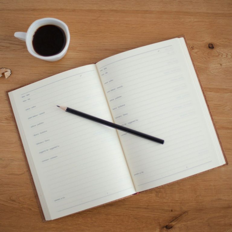 Ein offenes Notizbuch mit einer Bleistift und einer Tasse Kaffee daneben.