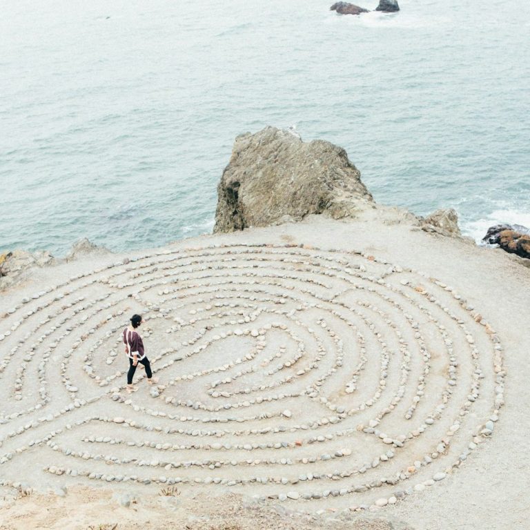 Eine Person geht in einem Steinglabyrinth an der Küste entlang.