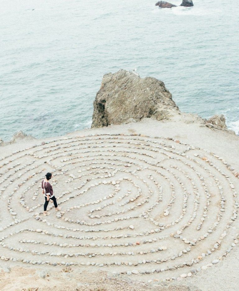 Psychotherapie und Coaching für Klarheit, Selbstwert und Veränderung Eine Person geht in einem Steinglabyrinth an der Küste entlang.